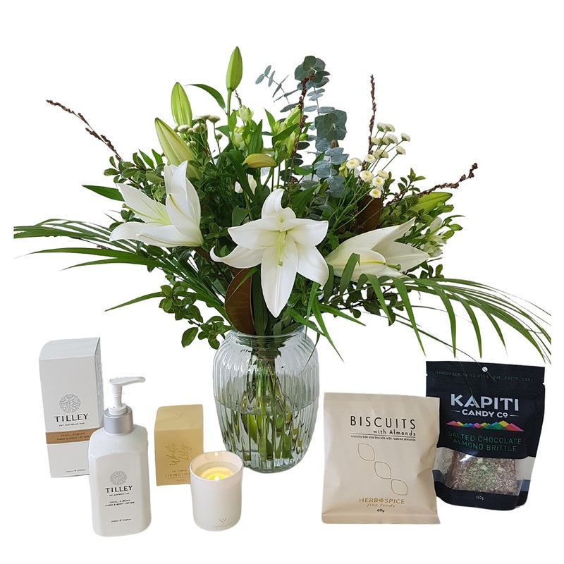 white lily posy in a glass vase with pamper products and tasty treats, 